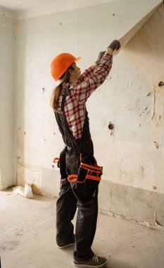 Erkek müteahhit eski duvar kâğıtlarını duvardan söküyor. Ev dekorasyonu sırasında. Kapalı alanda elle tamir işlemi yapıyor.