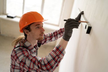 Duvara kurşun kalemle işaret bırakan profesyonel bir inşaatçı. Eğimi ruh seviyesiyle ölçüyor. Boşluğu kopyala