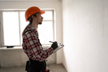 Kemerinde iş aletleri ve apartman yenileme panosu olan genç bir inşaatçı. Onarım, inşaat ve inşaat kavramı