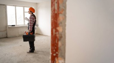 İnşaatçı, inşaat işçisi ya da tamirci mavi tulumlu ve koruyucu kasklı. Eski apartman dairesinde tadilata hazır bekliyor. Pankart. Boşluğu kopyala