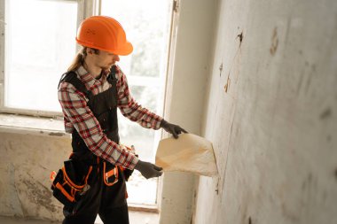 Genç inşaatçı ya da tamirci ev onarım işleri sırasında duvar kağıtlarını soyuyor. Boşluğu kopyala
