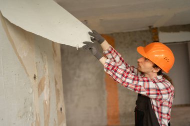 Miğferli müteahhit duvardaki eski duvar kâğıtlarını söküyor yenileme ve iç yenileme için apartman hazırlıyor. Boşluğu kopyala