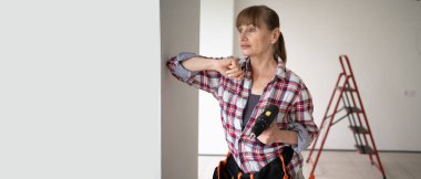 Orta yaşlı, düşünceli bir tamirci. Alet kemeri takmış, elinde elektrikli matkap var. Ev tamiri yapıyor. Pankart. Boşluğu kopyala