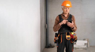 İnşaat alanında sosyal hizmetleri okurken cep telefonu kullanan yaşlı inşaatçı. Uzayı kopyala Pankart