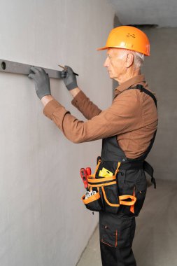 Yaşlı erkek müteahhit, ruh seviyesini kullanarak duvarın seviyesini kontrol ediyor. Meslek, inşaat ve inşaat kavramı