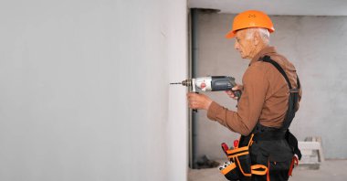 Duvarda matkapla delme deliği açan profesyonel mimar ya da tamirci. Yaşlı inşaat işçisi. Pankart. Boşluğu kopyala