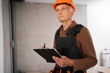 Erkek mühendis güvenlik kaskı takıyor. Yeni evde elinde bir pano var.