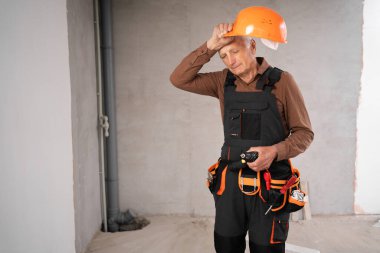 Üniformalı kıdemli müteahhit tamir evinde dikiliyor, bıkkınlık işçisi yorgun. Tamir, ev tadilatı ve inşaat. Boşluğu kopyala