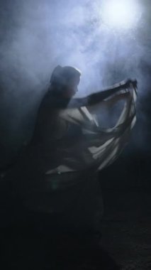 Gece dumanlı sahnede dans eden beyaz elbiseli bir dansçı. Dikey video