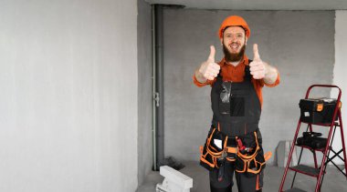 Pozitif sakallı bir tamirci ya da koruyucu miğfer ve tulum giymiş bir müteahhit. Başparmağını kaldırıp kameraya bakıyor. İnşaat malzemeleriyle odada iyilik olup olmadığını kontrol ediyor. Yapı ve onarım kavramı