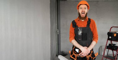 Sakallı bir tamirci ya da miğferli bir müteahhit ve tulumlu. İnşaat malzemeleriyle odada dilini gösteriyor. Yapı ve onarım kavramı