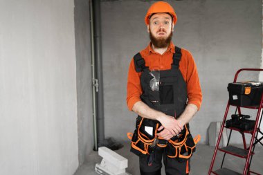 Sakallı tamirci ya da miğferli ve tulumlu müteahhit inşaat malzemeleriyle odada yanak üflüyor. Yapı ve onarım kavramı