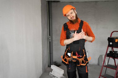 Sakallı bir tamirci ya da miğfer ve tulum giymiş bir müteahhit. İnşaat malzemeleriyle odada sevgi ifadesi olan bir kalbe dokunuyor. Yapı ve onarım kavramı