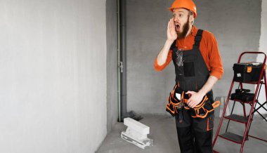 Sakallı bir tamirci ya da miğferli ve tulumlu bir tamirci el ele tutuşup bina malzemeleriyle odadaki reklamlara dikkat çekiyordu. Yapı ve onarım kavramı