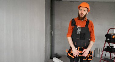 Kasklı ve tulumlu genç sakallı müteahhit evi yenilerken kameraya bakıyor. Boşluğu kopyala