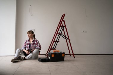 Ev onarımı yapan orta yaşlı profesyonel bir tamirci. Alet çantasının yanında oturuyor. Boşluğu kopyala