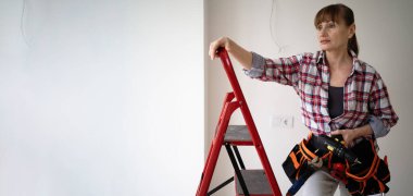 Evde tadilat yapan bir kadın elinde matkapla merdivende dikiliyor. afiş, boşluğu kopyala