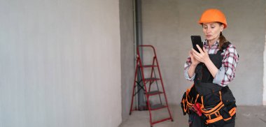 İşçi kadın tadilat odasında sabit şapka takıyor cep telefonu kullanıyor. Tamir, yenileme ve inşaat konsepti. Pankart. Boşluğu kopyala