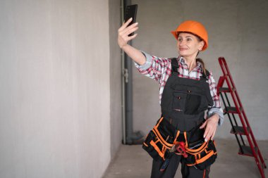 İnşaat alanında kadın inşaatçı ya da mimar görüntülü görüşme yapıyor. Boşluğu kopyala
