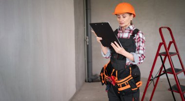 İnşaat alanında elinde not defteri olan kasketli bir kadın. Onarım, inşaat, yenileme ve bakım konsepti