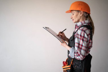 Kadın tamirci ya da miğferli bir tamirci beyaz arka planda panoya notlar yazıyor. Meslek, inşaat ve inşaat kavramı. Boşluğu kopyala