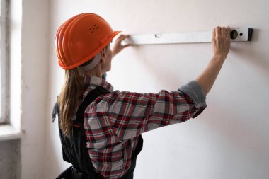 Koruyucu kask takan kadın inşaat işçisi veya inşaatçı, yenileme veya inşaat çalışmaları sırasında ölçüm duvarı olarak ruh seviyesini kullanır. Arka plan