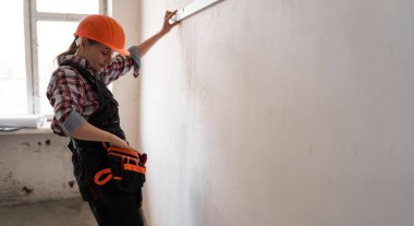 Sivil mühendis kadın başlık ve alet kemeri takıyor. Duvarı ölçüyor. Kalem seviyesine ulaşıyor. Pankart