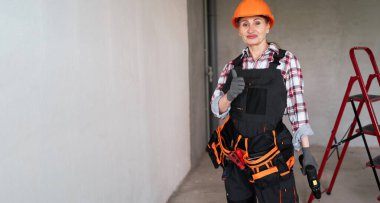 Tulumlu ve koruyucu kasklı kadın müteahhit portresi tadilat altında evde duruyor. Pankart. Hızı kopyala