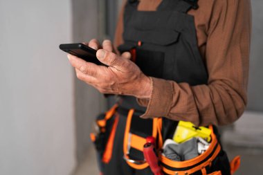 Akıllı telefon ve kemerle ev içi iş aletleri olan inşaatçı ellerinin yakın çekimi. Tamir, inşaat ve inşaat kavramı. Boşluğu kopyala