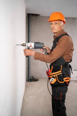 İnşaat işçisi elektrikli matkapla duvarda delik açıyor. İnşaat işleri, ev onarımı ve apartman yenileme çalışmaları sürüyor