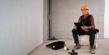 İnşaat alanında elinde bir pano olan üzgün inşaatçı bitmemiş evdeki eğri büğrü duvar yüzünden hayal kırıklığına uğramış. Tadilat ve inşaat sorunları kavramı. Pankart