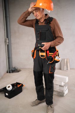 Üniformalı kıdemli müteahhit tamir evinde dikiliyor, bıkkınlık işçisi yorgun. Tamir, ev tadilatı ve inşaat. Boşluğu kopyala