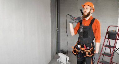 Sakallı erkek inşaat işçisi ya da elinde elektrikli matkap ya da yeni evde duran bir pervane tutan inşaatçı. Meslek, inşaat ve inşaat konsepti. Pankart. Boşluğu kopyala