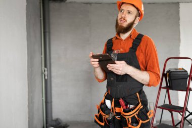 Odada tabletli ve kemerli aletleri olan bir müteahhit. İnsanlar, teknoloji, inşaat ve onarım kavramı