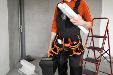 Evde çalışmaya hazırlanırken alet kemeri takan tamirci alet çantası ve planlar tutuyor. Tamirat, yenileme ve tadilat işleri..