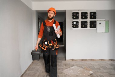 Kasklı tamirci alet çantası tutuyor ve tadilat sırasında evin koridorunda duruyor. İnşaat, ev bakımı, tamirat ve kapalı alanda onarım işi kavramı..