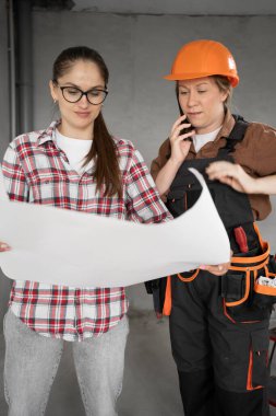 Bina, ev tadilatı ve tamir konsepti. Katı şapkalı bir kadın müteahhit. Kağıt plan kullanarak müşteri ya da apartman sahibine yenileme projesi gösteriyor. Boşluğu kopyala