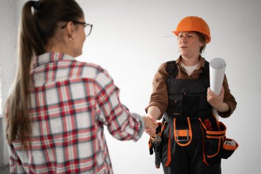 Kadın daire sahibi ve inşaat işçisi ev onarım projesini tartışırken el sıkışıyor. Boşluğu kopyala