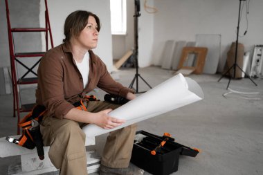 İşyeri planında çalışan tamirci kadın inşaat alanında oturmuş konut geliştirme projesini okuyor. Boşluğu kopyala.