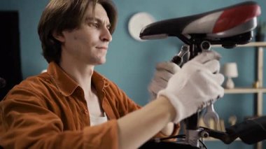 Evde bisiklet koltuğunu tamir eden günlük giysili bir adam. Boşluğu kopyala