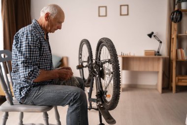 Emekli beyaz bir adam evde bisikletini tamir eder. Özenli yaşlı bir adam, bisikletini iyi durumda tutarak arka tekerleğe bakar. Boş zaman ve arama..