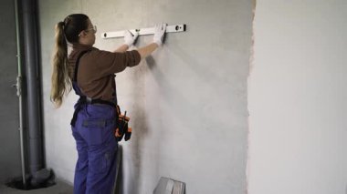 Tulumlu kadın tamirci. Ev onarımı yapıyor. Ruh seviyesiyle duvarları ölçüyor. Ev yenileme ve onarım konsepti