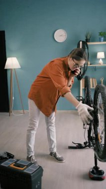 Woman bike mechanic calling repair service for advice over smartphone at home. Concept of DIY support, consultation, technical help and smart transport maintenance.