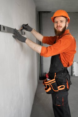 İnşaat işçisi ya da mühendis duvarı ruh seviyesiyle ölçer. Kameraya gülümsüyor. Boşluğu kopyala