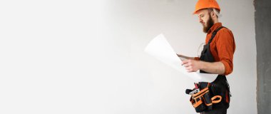 Bearded builder or engineer holding blueprint paper plan for new house construction. Architect with paper project against white wall. banner. Copy space