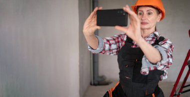 Orta yaşlı müteahhit, akıllı telefondan sosyal medya için fotoğraf içeriği kaydediyor. Onarım, inşaat ve inşaat konsepti. Pankart