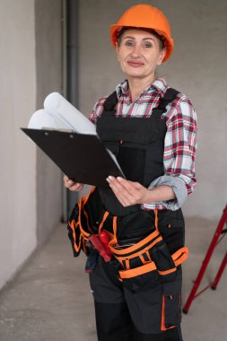 İnşaatçı kadın işçi. Orta yaşlı kadın ustabaşı koruyucu miğferli kağıt ve pano projeli mühendis. Boşluğu kopyala