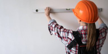 Koruyucu kask takan kadın inşaat işçisi veya inşaatçı, yenileme veya inşaat çalışmaları sırasında ölçüm duvarı olarak ruh seviyesini kullanır. Boşluğu kopyala