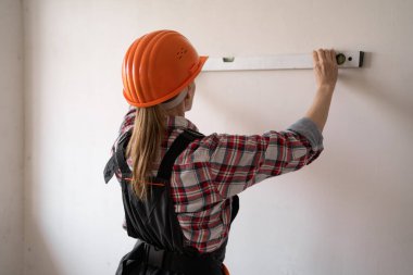 Kadın inşaat işçisi yeni evin duvarlarını ruh seviyesiyle ölçüyor. Arka plan