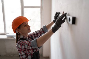 Tamir ve inşaat konsepti. Miğferdeki kadın mühendis ya da müteahhit evdeki duvar ölçümlerini kontrol ediyor. Boşluğu kopyala